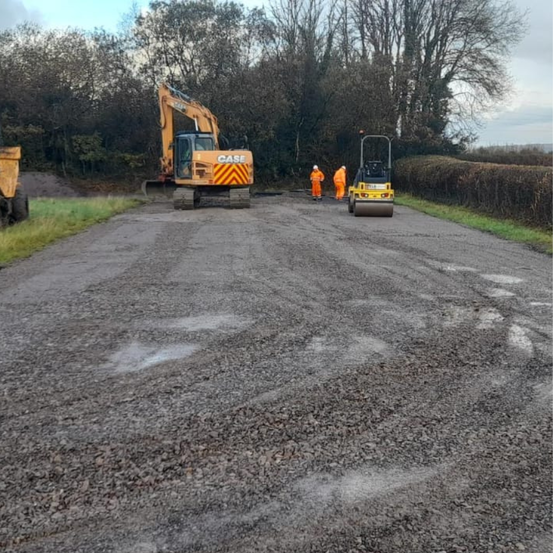 Site enabling works using a orange JCB. Trees and bushes on the edge. Gravel land